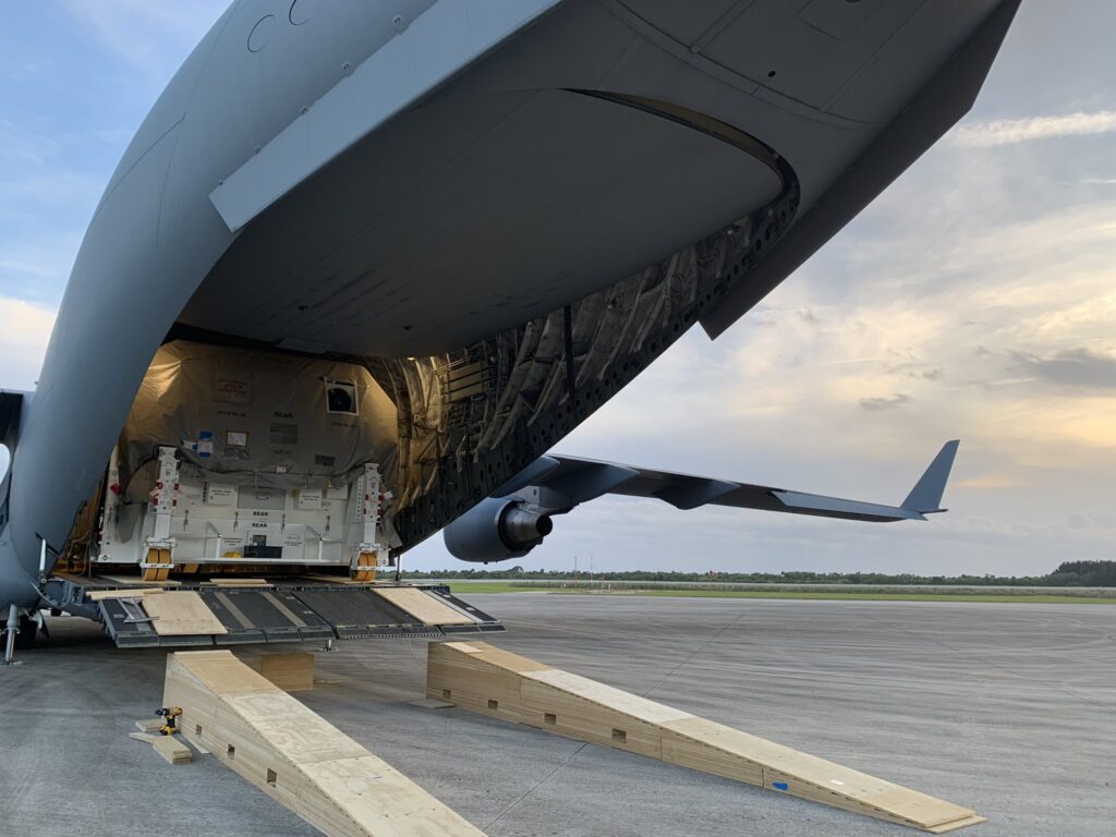 A white box containing the Psyche spacecraft in the open back of a large transport aircraft.